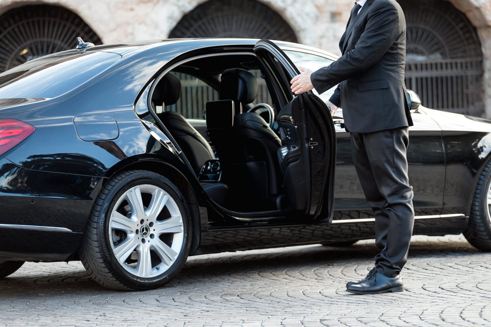 Chauffeur in a dark suit opening the rear door of a black executive sedan